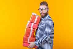 惊讶年轻的赶时髦的人的家伙眼镜持有大堆栈礼物盒子黄色的背景概念一年圣诞节礼物广告空间
