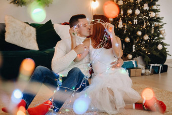 快乐结婚了夫妇坐着首页地板上圣诞节树接吻