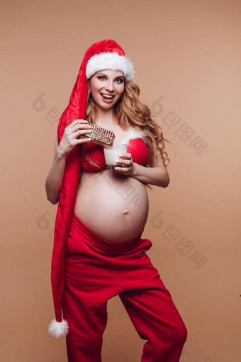孤立的<strong>图片</strong>年轻的美丽的怀孕了女人<strong>圣诞老人</strong>服装吃图拉姜饼牛奶