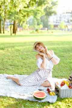 年轻的美丽的女人坐着公园格子水果草背景