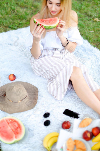 高加索人金发女郎女人坐着格子水果他吃西瓜草背景