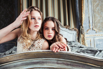 漂亮的双胞胎妹妹金发碧眼的卷曲的发型女孩奢侈品房子室内丰富的年轻的人概念