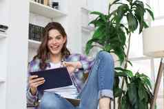微笑年轻的女坐着地板上生活房间学生研究首页工作平板电脑