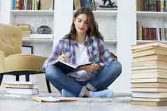 年轻的女学生研究首页写作文章出版坐着地板上舒适的国内室内包围桩书