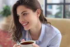 微笑年轻的女坐着扶手椅生活房间持有杯咖啡