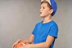 可爱的男孩篮球球员站灰色的背景