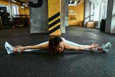 年轻的灵活的健身女人运动服装坐着地板上健身房练习横向线伸展运动肌肉锻炼