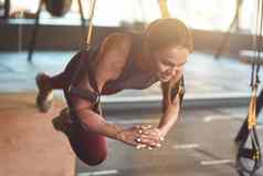 工作硬年轻的运动健身女人运动服装trx锻炼工业健身房工作健身肩带悬架培训概念