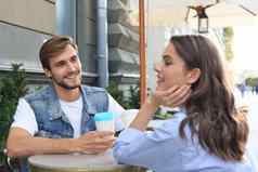 有吸引力的年轻的夫妇爱喝咖啡坐着咖啡馆表格在户外
