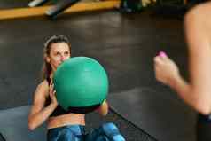 年轻的运动型女人运动服装ABS练习锻炼健身球健身房援助个人教练
