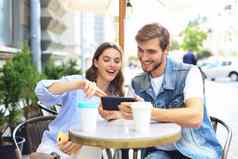 有吸引力的年轻的夫妇爱喝咖啡坐着咖啡馆表格在户外移动电话