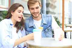有吸引力的年轻的夫妇爱喝咖啡坐着咖啡馆表格在户外移动电话