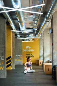 垂直拍摄年轻的运动女人运动服装坐着瑜伽席健身房窗口气候变暖伸展运动身体锻炼
