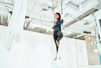 爱丽儿瑜伽年轻的高加索人女人运动服装练习飞瑜伽工作室站腿白色吊床冥想