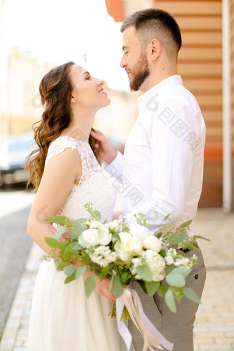 快乐英俊的新郎拥抱的未婚妻保持花穿白色衣服