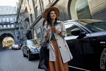 享受购物年轻的快乐时尚的女人纸购物袋智能手机微笑站黑色的奢侈品车城市街