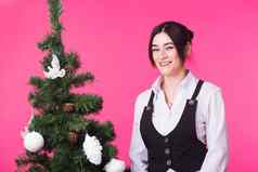 年轻的快乐女人圣诞节树粉红色的背景