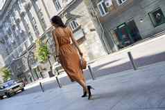 完整的长度年轻的时尚女人穿长浪漫的衣服高非常鞋子走城市街道后视图