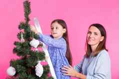 假期家庭圣诞节概念妈妈。女儿装修圣诞节树粉红色的背景