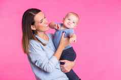 家庭母亲育儿人孩子护理概念快乐妈妈。持有可爱的婴儿粉红色的背景