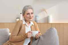 快乐成熟的女人休息舒适的沙发喝咖啡茶放松舒适的沙发上首页享受热饮料