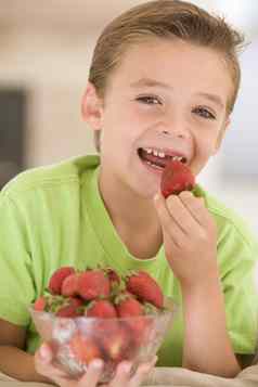 年轻的男孩吃草莓生活房间微笑