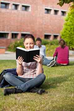 女学生阅读书坐着草