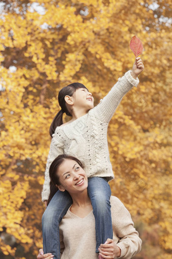 女儿骑多加利用母亲的肩膀享受秋天叶子