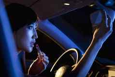 年轻的美丽的女人传统的中国人衣服把口红后视图镜子车晚上