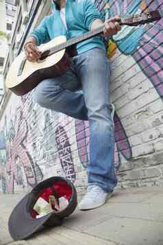 年轻的街音乐家玩吉他街头卖艺钱前面墙涂鸦