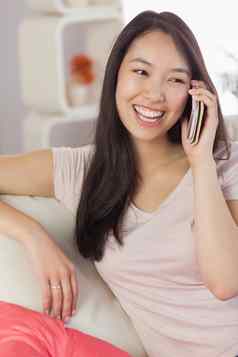 漂亮的亚洲女孩会说话的智能手机沙发上
