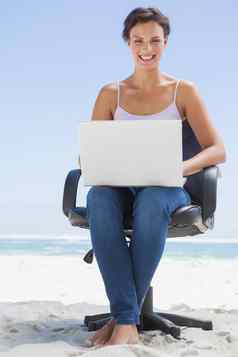 漂亮的浅黑肤色的女人移动PC海滩坐着旋转椅子