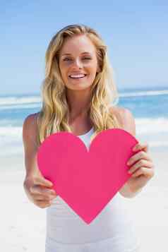 微笑金发女郎显示粉红色的心海滩