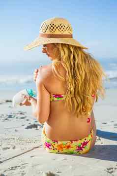 华丽的女人坐着海滩遮阳帽应用防晒霜