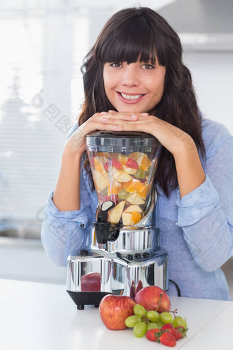 微笑浅黑肤色的女人倾斜榨汁机完整的水果