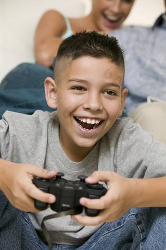 特写镜头快乐的男孩玩视频游戏快乐模糊妈妈。背景首页