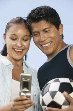 年轻的夫妇移动电话男人。持有足球球清晰的天空
