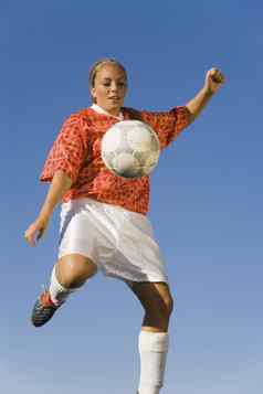 年轻的女足球球员踢足球蓝色的天空