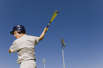 年轻的棒球球员摆动蝙蝠蓝色的天空