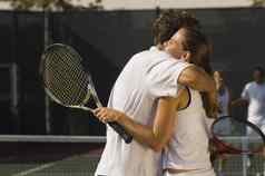 网球球员拥抱赢得匹配合作伙伴站背景