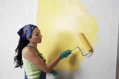 一边视图女人辊应用黄色的油漆墙