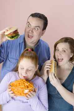 肥胖家庭吃垃圾食物孤立的粉红色的背景