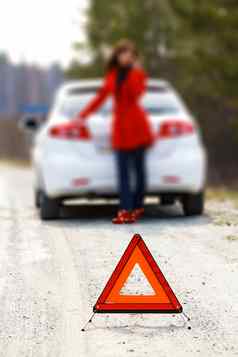 女人站破碎的车警告三角形标志