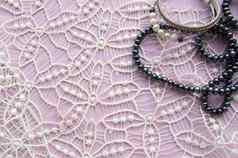 躺平粉红色的背景华丽的花边闪闪发光的项链黑色的珍珠时尚的手镯美时尚概念