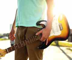 年轻的赶时髦的人蓝色的t恤吉他站路对比阳光眩光夏天一天在户外