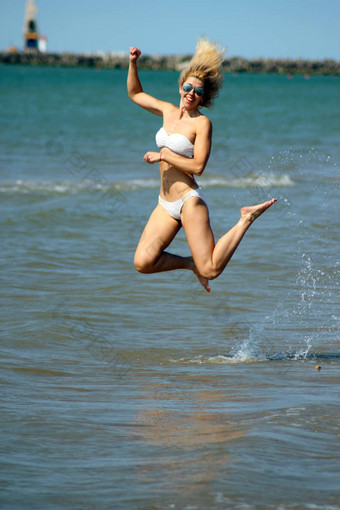 微笑晒黑金发女郎白色比基尼太阳镜使跳水桑迪海滩波罗的海海海岸