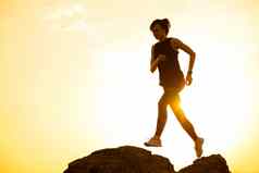 美丽的女人跑步者跳岩石山小道热夏天日落体育运动活跃的生活方式