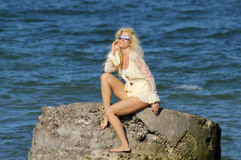 晒黑金发女郎白色衣服太阳镜坐在石头海岸波罗的海海阳光明媚的一天