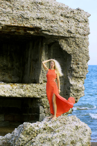 晒黑金发女郎女孩红色的衣服站石头废墟堡背景波波罗的海海