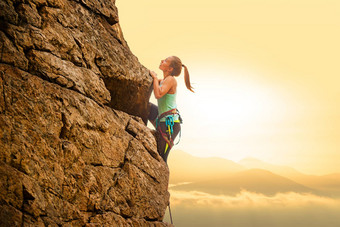 美丽的女人攀爬岩石多雾的日落山冒险极端的体育运动概念